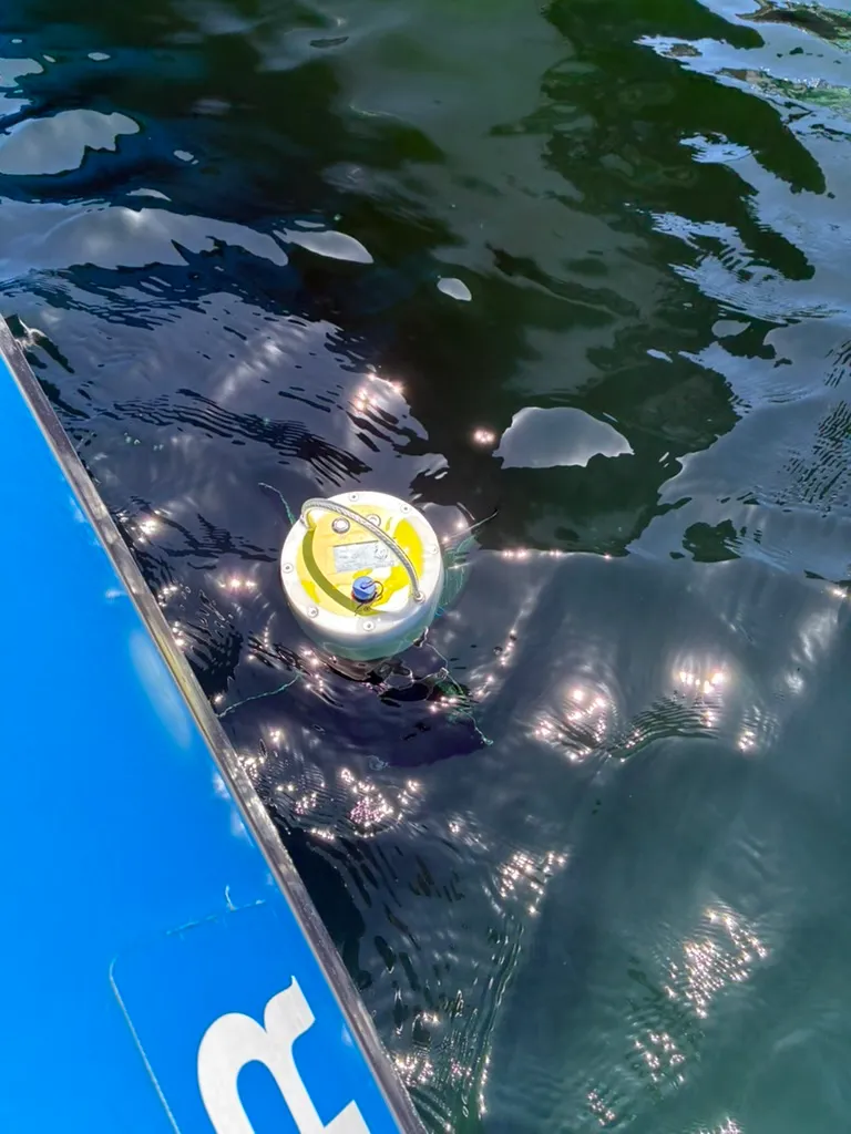 The DrifterBuoy CMU-30 floating in the water alongside a boat, its yellow top deck just above the surface.