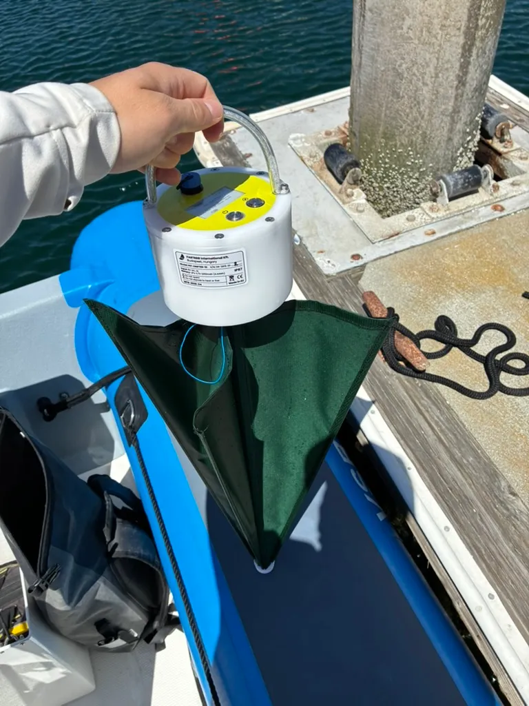 The buoy held by its handle with the green drogue screwed onto its underside, hanging open below the housing.