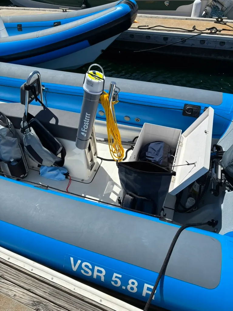 The grey Fastrrr tube mounted upright against the console of a blue RIB, holding the buoy with its handle at the top, a coiled yellow retrieval line hanging beside it.